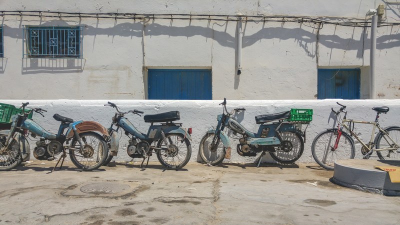 a row of old fashioned motorcycles beside a bike lined up against the wall in a rural area, tunisian motor club 4k
