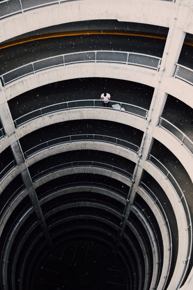 young person sits with back against railing of spiraling building, spiraling building 4k