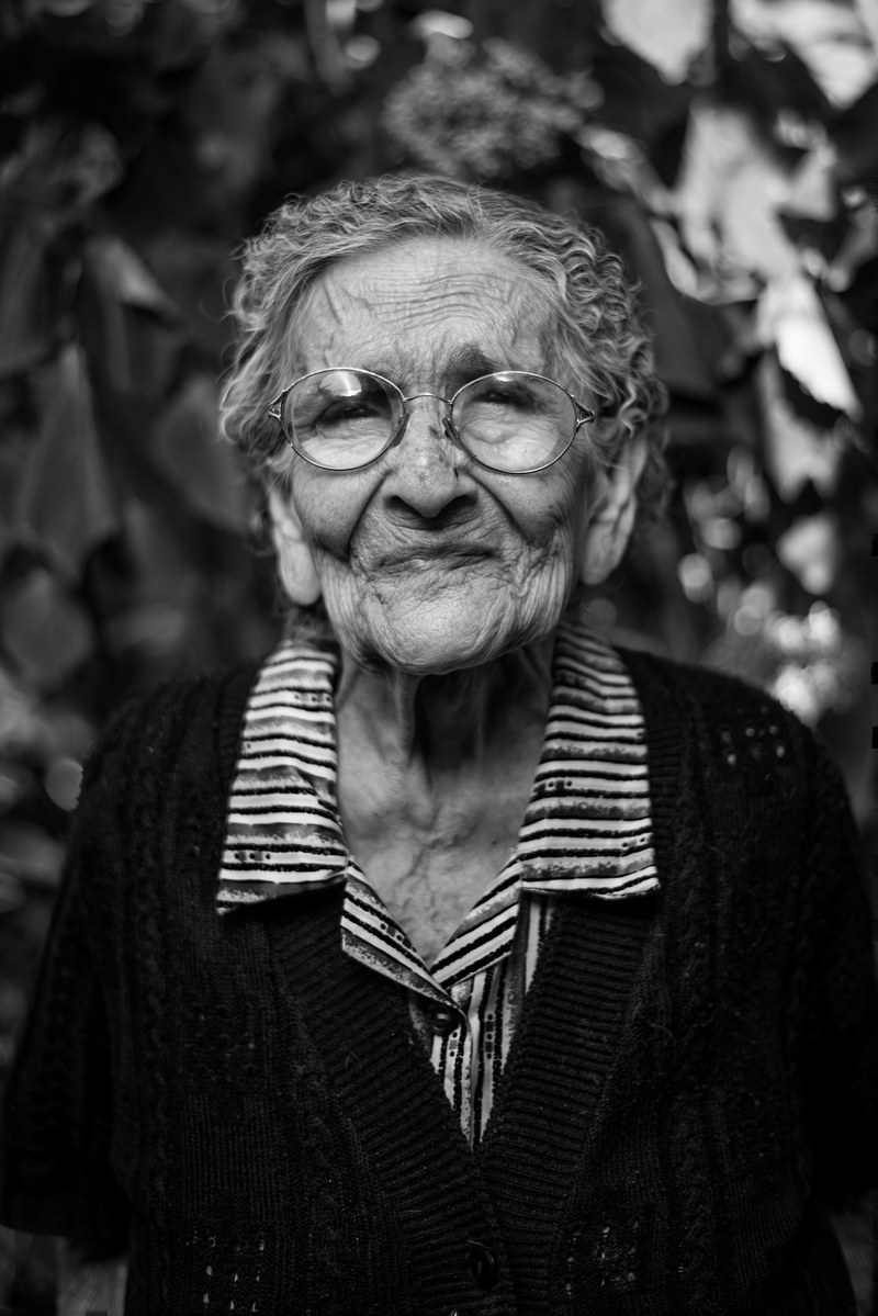 an old retired women with circular glasses in a black and white close up macro portrait, old woman smiling_ 4k