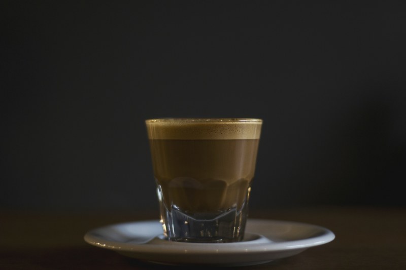 espresso in a clear glass on a white saucer with a black featureless background, espresso on a white saucer 4k