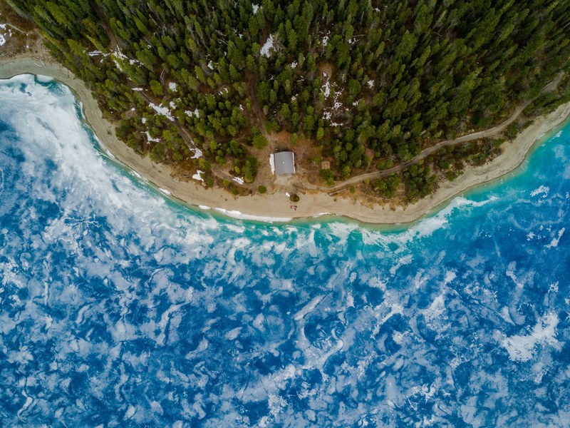 a drone shot of a sandy beach and a forest near a blue lake, canadian beach 4k