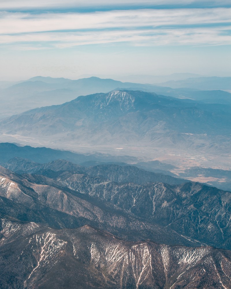 a drone shot of a vast mountain valley behind long mountain ridges, mountain valley in the distance 4k