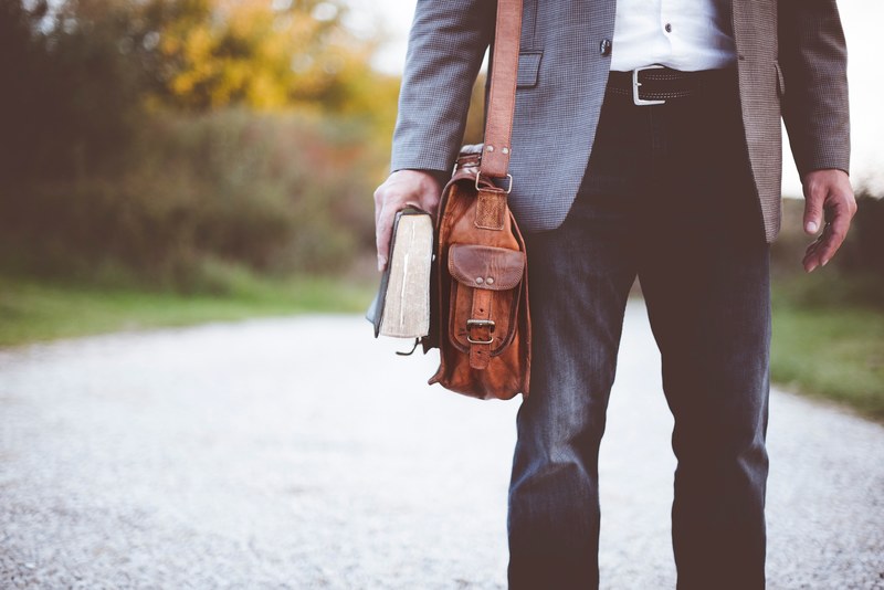 a low shot of an elegantly dressed man with a leather bag holding a book in his hand, man with leather bag and book 4k