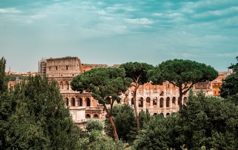 the ruins of the roman colosseum behind green trees, the majestic colosseum in rome_ 4k