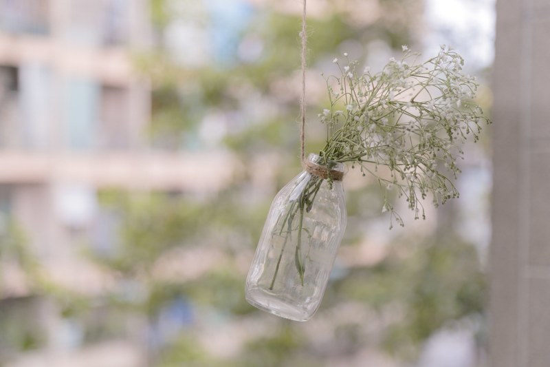 a glass bottle with white babys breath flowers hanging up from a string, babys breath posy on a string 4k