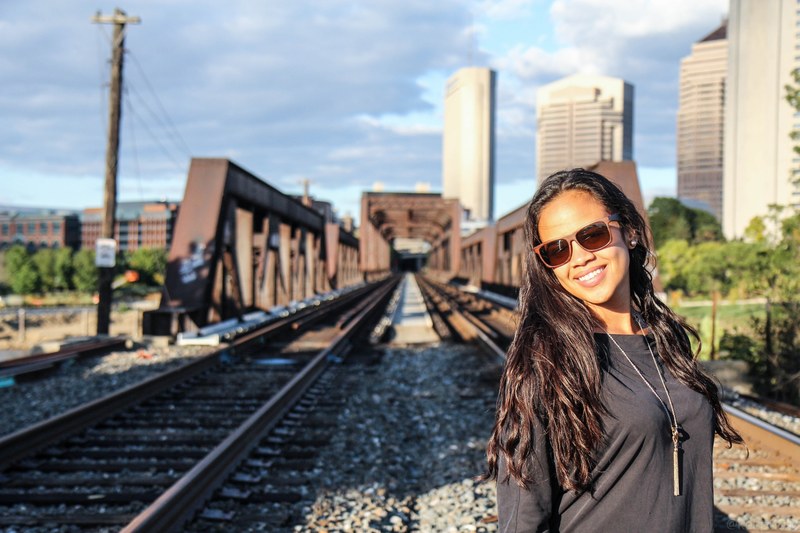 woman in sunglasses with a long necklace smiles in front of train tracks in the city, woman in front of train tracks 4k