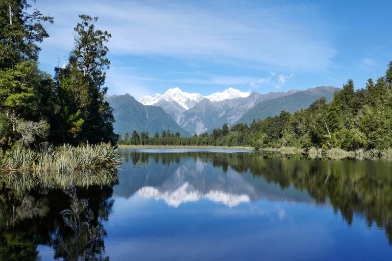 tall snowy mountains reflected in the still surface of lake matheson, the mirror lake 4k
