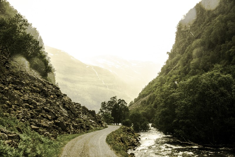 a winding road through the mountains bordered by a stream and a rock face, winding road through green mountains 4k