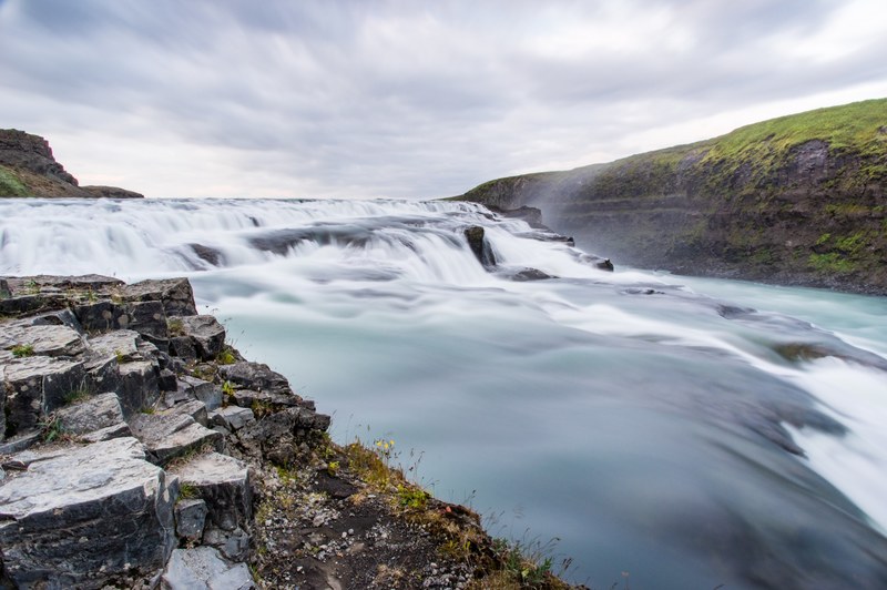 a low waterfall with foamy water flowing down between mossy rocks, waterfall in thingvellir 4k