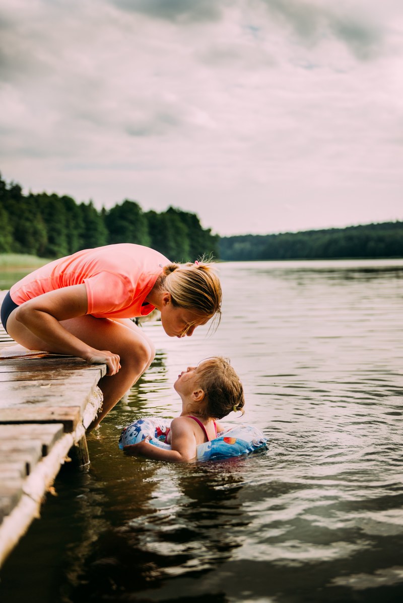 mother encourages her child swimming in a lake, family lake vacation 4k