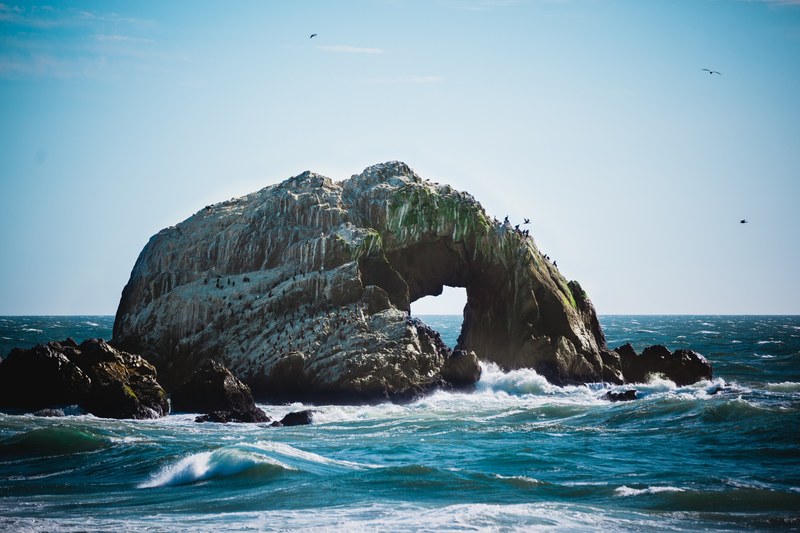 flocking birds on a rocky arch in the middle of the sea, natural rock arch in the sea 4k
