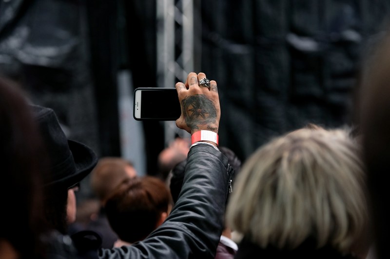 a man with a tattooed hand holding a smartphone while standing in a crowd, _crowd holding smartphone 4k