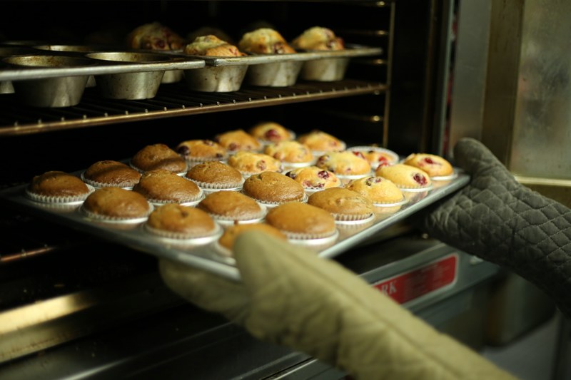 a person with oven mitts is loading the oven with a tray of muffins, muffins coming out of the oven 4k