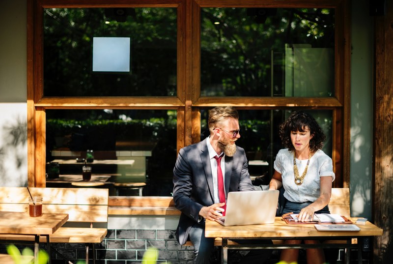 a man and a woman sitting together at a computer outside of a coffee shop for a business meeting, man and woman business meeting 4k