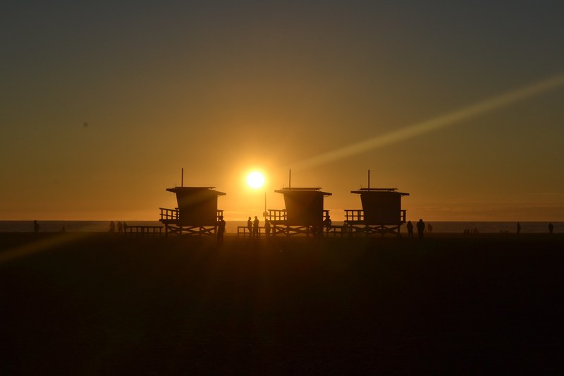 sun setting behind the silhouettes of three lifeguard stations at venice beach, lifeguard stations at sunset 4k