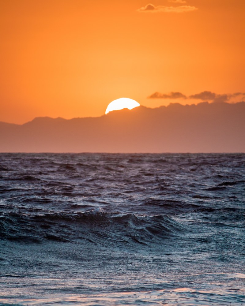 setting sun disappearing behind clouds over a rough sea, chasing sun 4k
