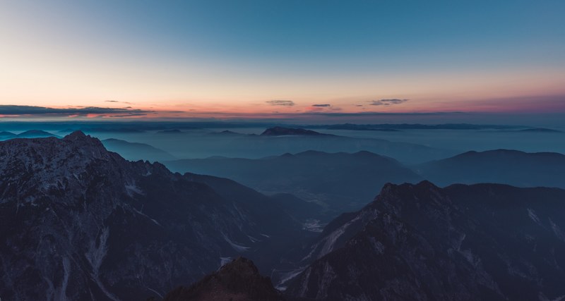 a hazy mountainous landscape with sharp ridges and deep valleys during sunset, sunset over mojstrovka 4k