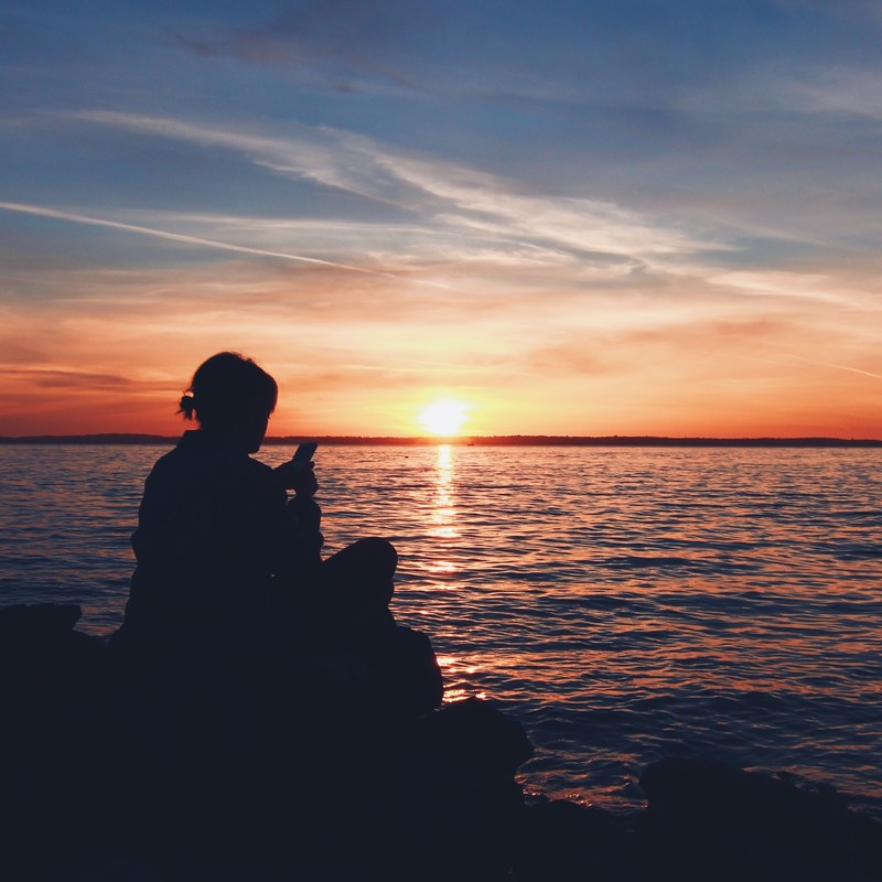 a silhouette of a person texting on their phone while watching the sunset, iphone beach sunset_ 4k