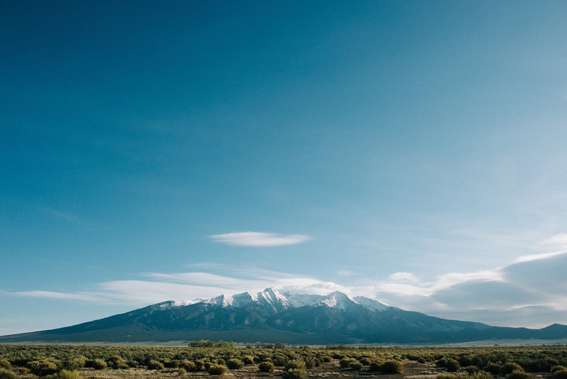 open blue sky above icy mountains surrounded by clouds and grassy ground, blue sky and icy mountains 4k