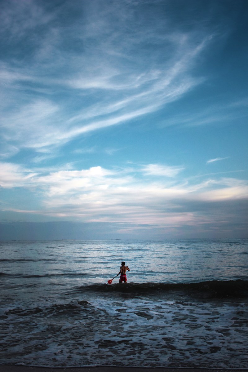 a paddleboarder on a calm sea beneath a blue dusky evening sky, evening paddleboarding 4k