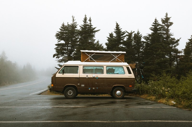 a cadillac camper van parked in a parking lot near a forest of pine trees, comfort in mobility 4k