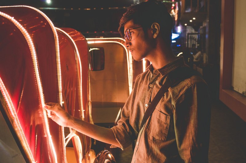 young hipster man looks at the lights lining a carriage on a dark city street, observing the lights 4k