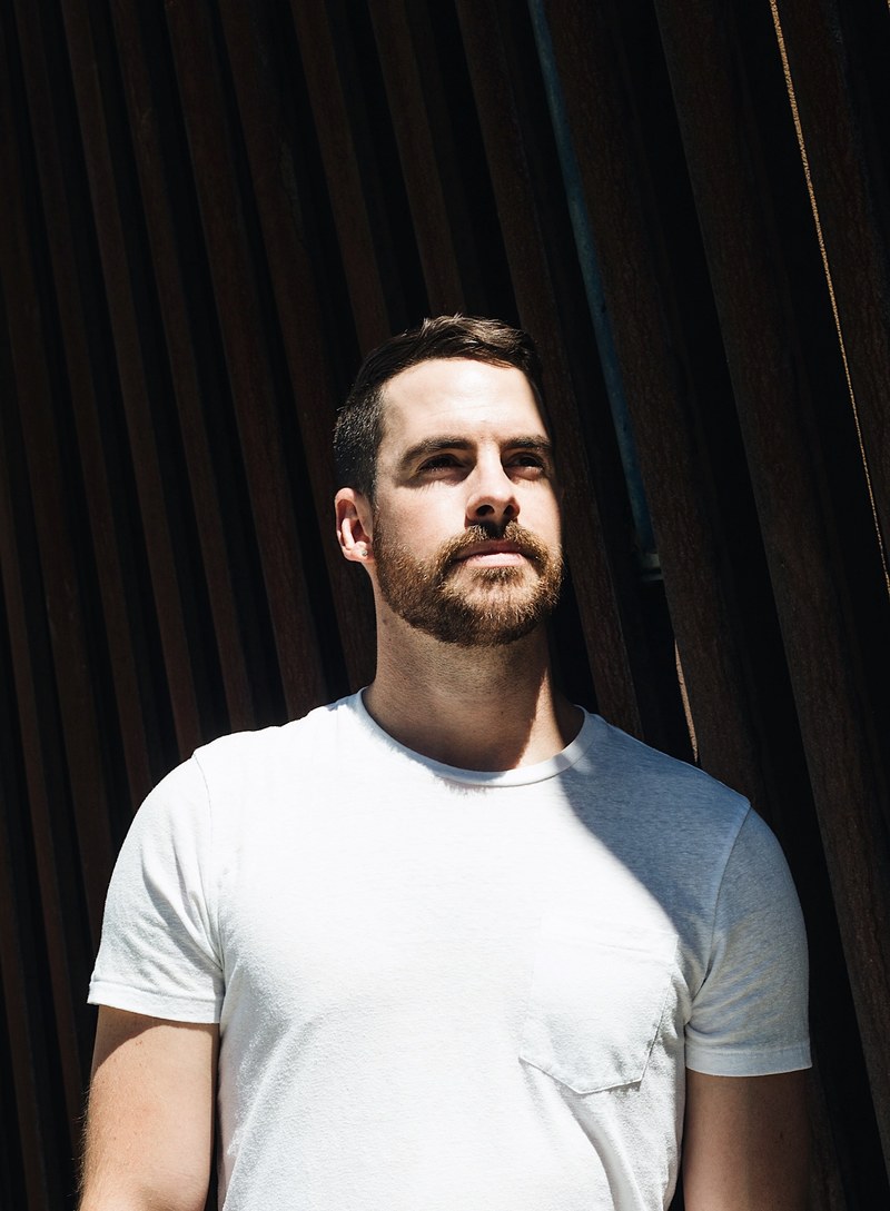 a bearded man in a t shirt leaning against a concrete structure, shadow play 4k