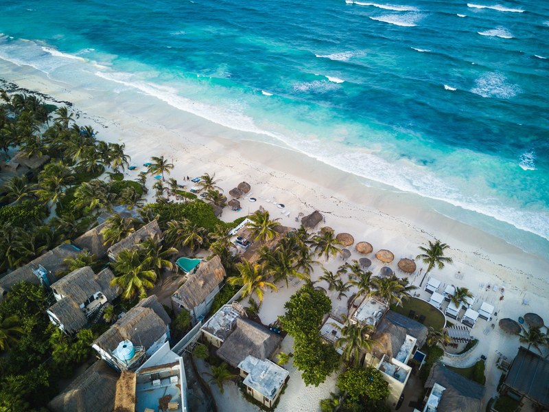 a drone shot of a resort umbrellas lounge chairs and the ocean in tulum mexico, washed up 4k