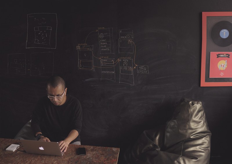 a man working on a laptop at a table near a chalkboard wall, designer at work 4k