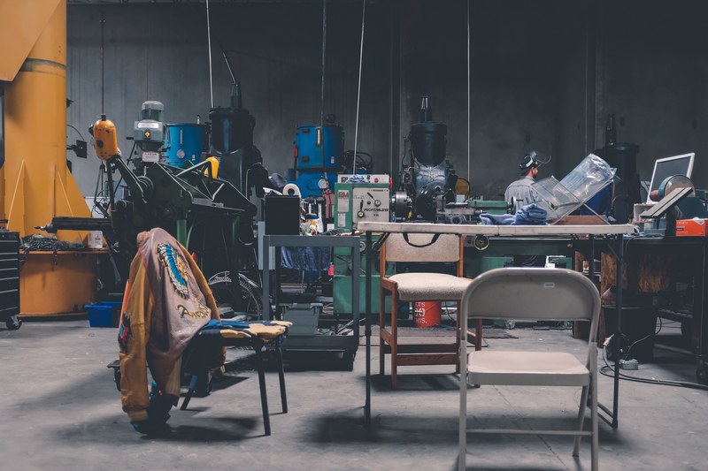 a man working in a messy workshop with a table chairs and various machines, man in a messy workshop 4k
