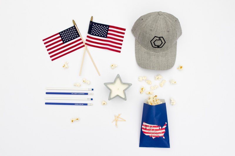 red white and blue americana gear on a white surface two small american flags a gray baseball hat pencils a star candle and popcorn, independence day 4k