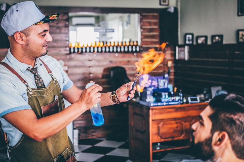 a man in an apron holds out a flaming utensil while another man looks on, looking toward a flame 4k