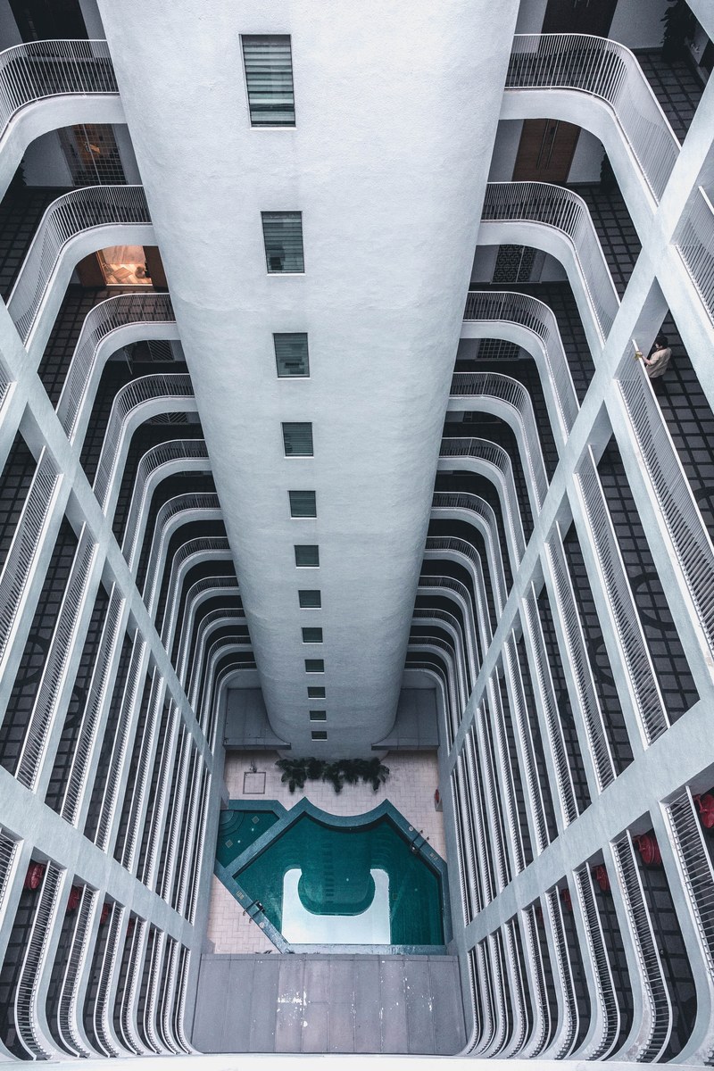 looking down from the top of a tall apartment building with many windows onto pool below, international plaza 4k