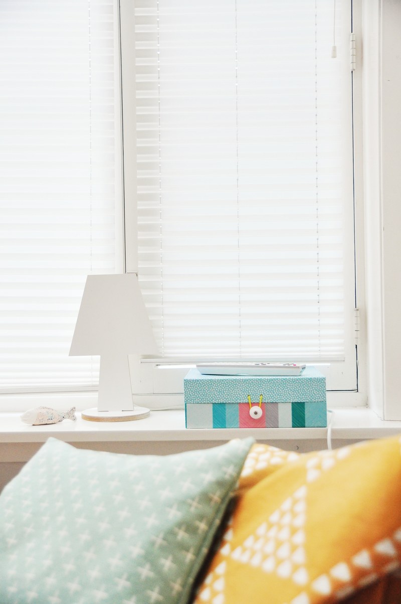 colorful cushions near a tv remote and a colorful box on a windowsill, cozy bed by a windowsill 4k