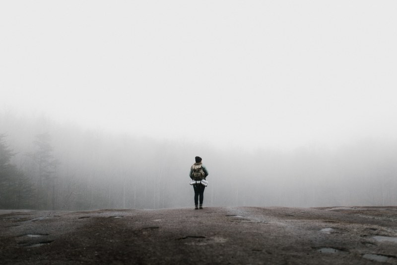 a woman standing on a rock wearing a backpack with her gear in it in the fog at stone mountain state park, musings of muir 4k