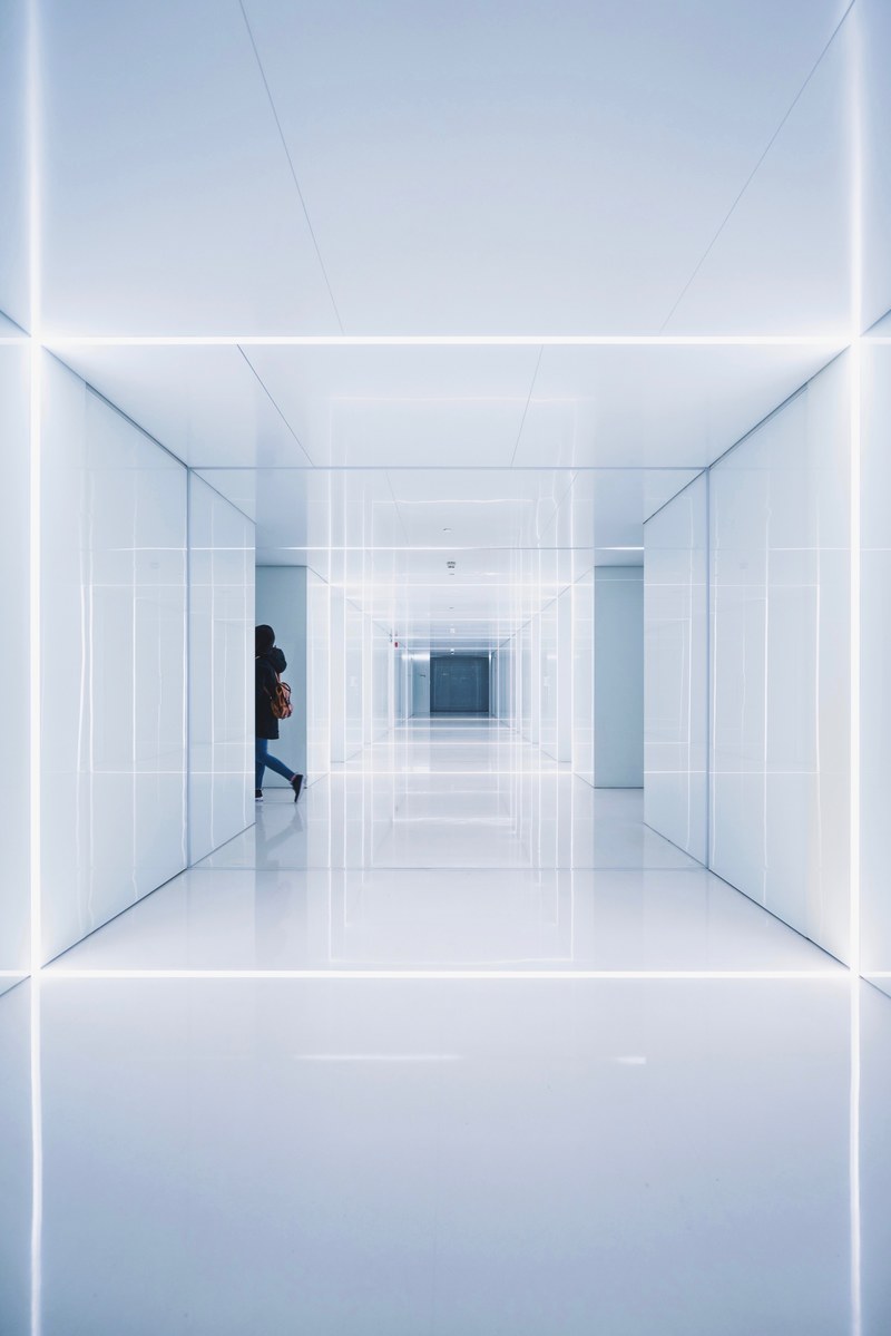 a woman disappearing behind a corner in a glossy white corridor, in time 4k
