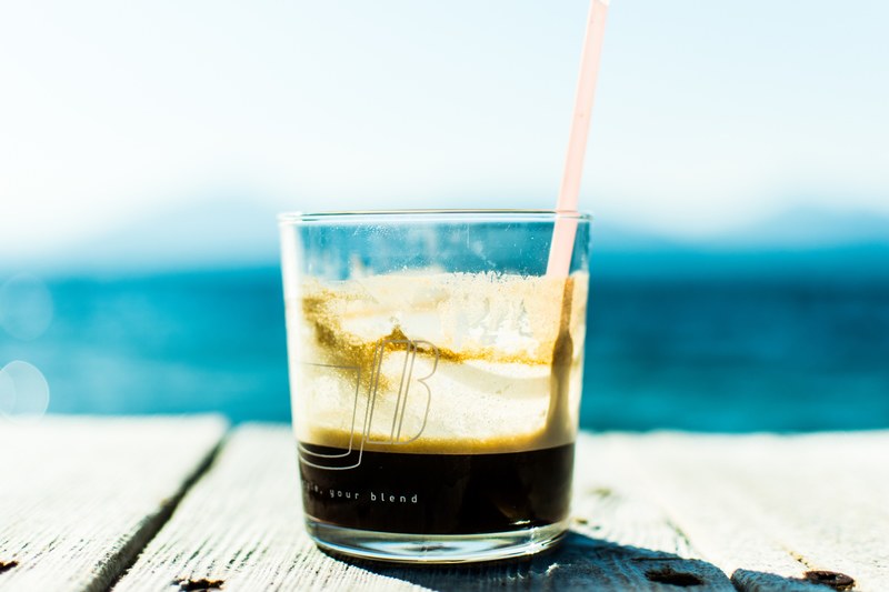 the macro view of a glass cup containing coffee and a straw on a table in greece, a glass cup of coffee 4k