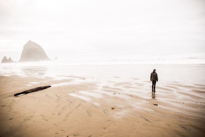 man standing on the sand beach coastline at cannon beach on a foggy day, it is done 4k