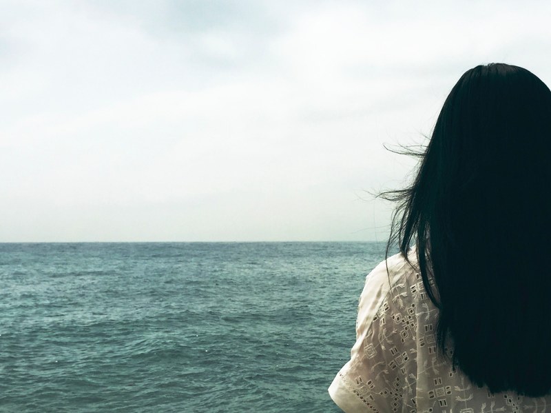 a dark haired woman looking off into the choppy sea stretching to the horizon, alone at sea 4k