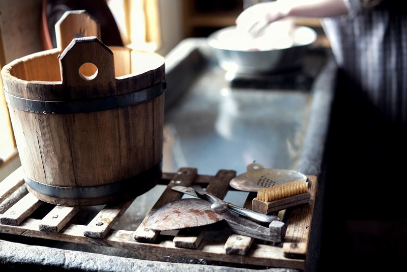 a wooden bucket brush and other cleaning supplies resting on a sink ledge while a person washes dishes in sturbridge, sturbridge dishes 4k
