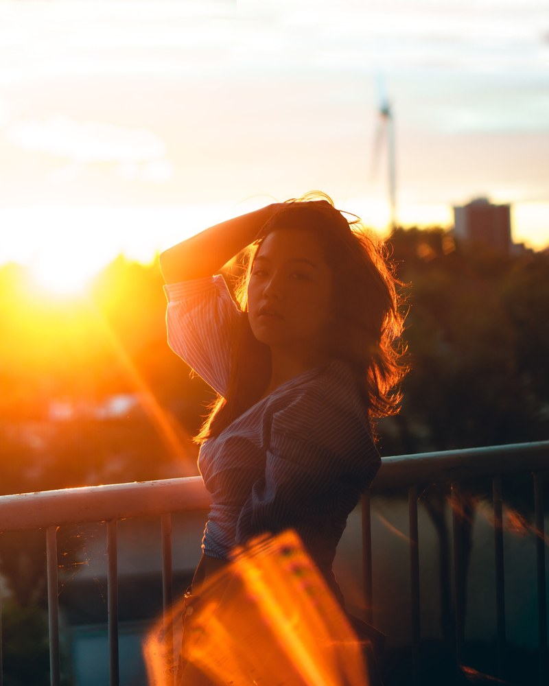 a woman in bright sunlight holds one hand in her hair by a railing, woman in bright sunlight 4k