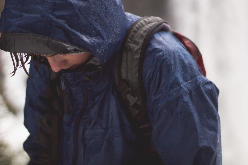 a wet person in a raincoat and backpack holds their head down, freezing 4k