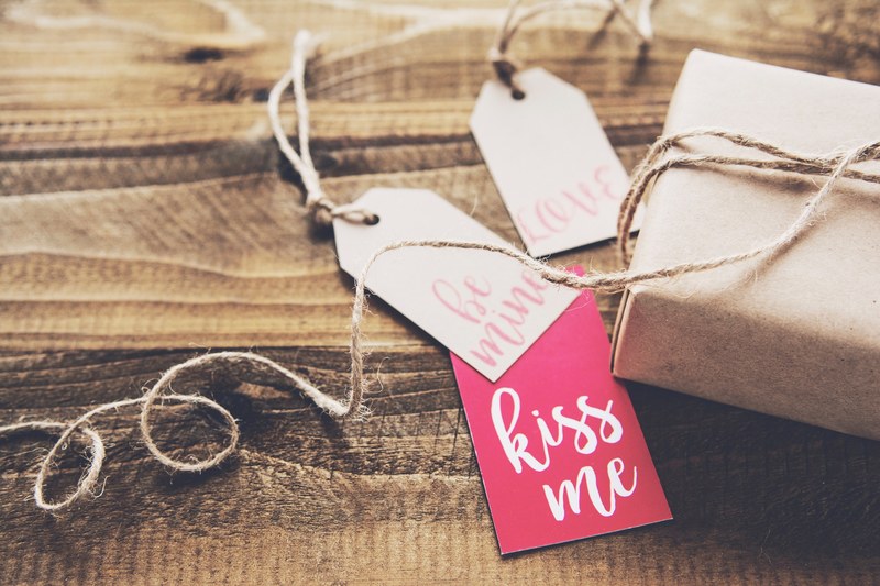 paper tags with kiss me written on one of them next to a wrapped gift, valentines day gift 4k