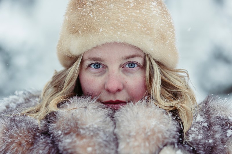 woman bundled up in a fur hat coat and mittens looks cold in the snow, frozen 4k