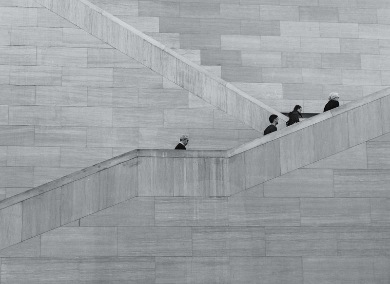 a black and white shot of people climbing up a tall concrete staircase, gloomy staircase 4k