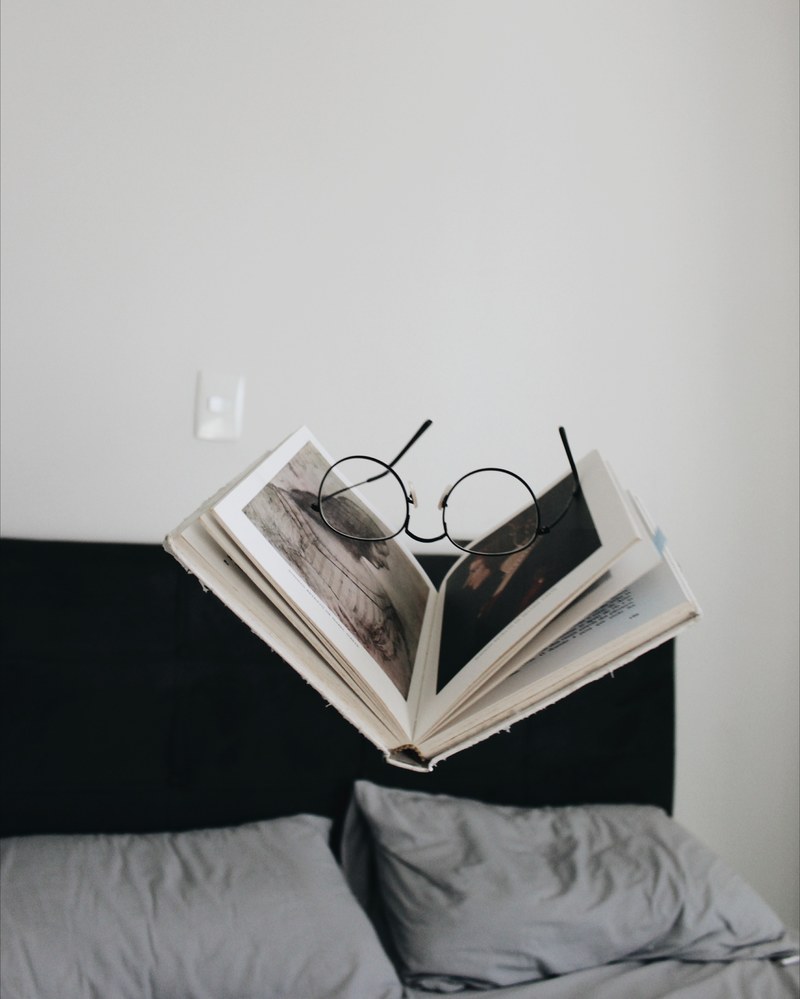 a pair of glasses on a half open book floating above a double bed, book and glasses over a bed 4k