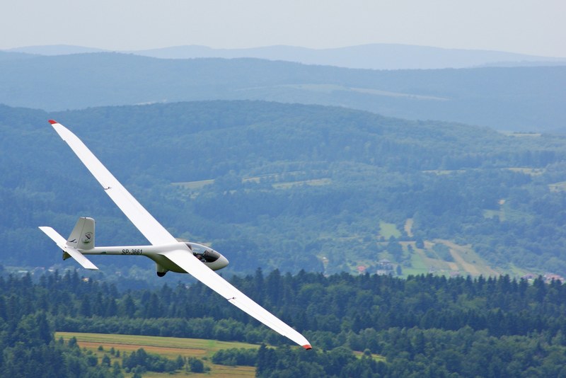 a white glider in flight over forested hills, gliding over the countryside 4k