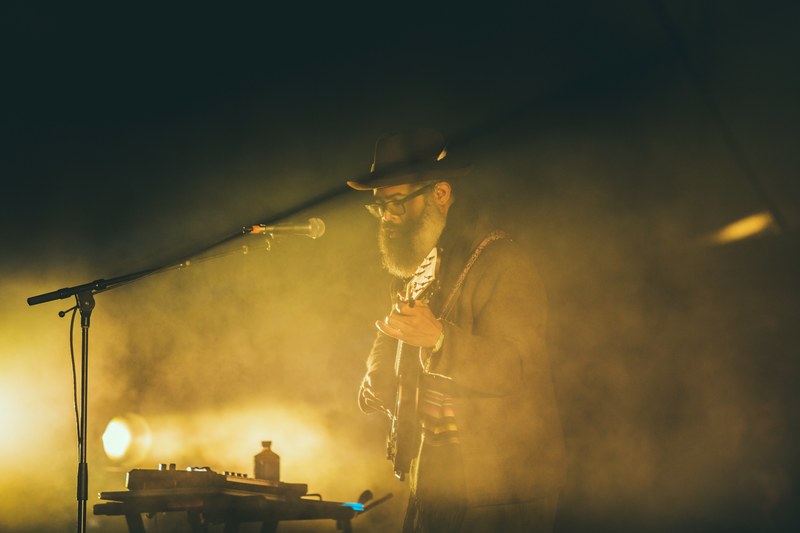 musician glows in yellow smoke and light on stage at a show, bearded guitar concert 4k
