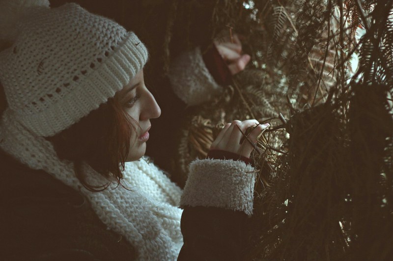 a woman in a knit cap peeking through dense needly branches, lost in the forest 4k
