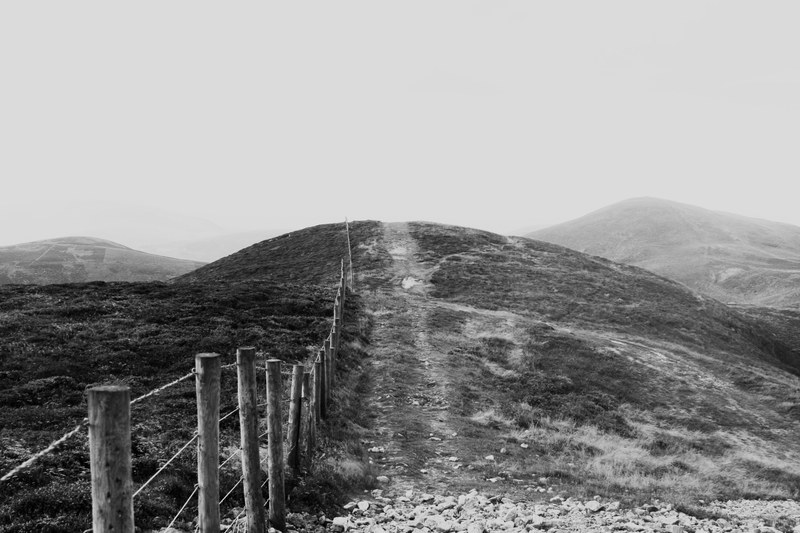 black and white shot of wire fence with wooden posts on grassy hills with clear sky, monochrome wire fence on hill 4k
